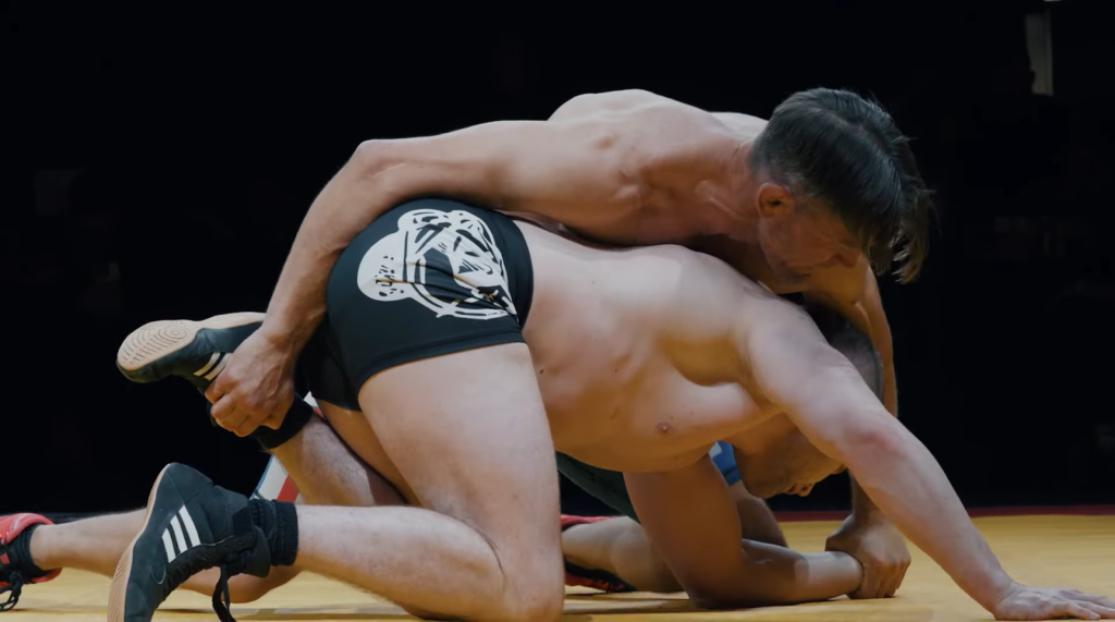two wrestlers fighting, one lying on the other and holding the opponent’s leg