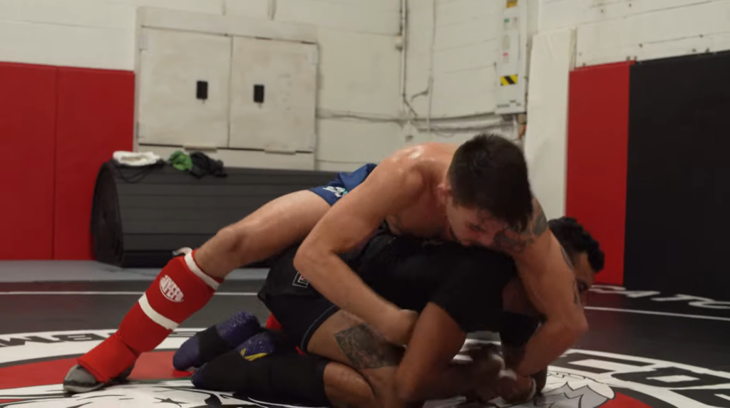two men fighting in the gym, one lying on the opponent and beats him
